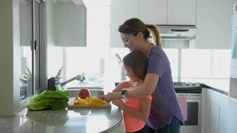 madre enseñando a su hija a cortar verduras en la cocina 4k
