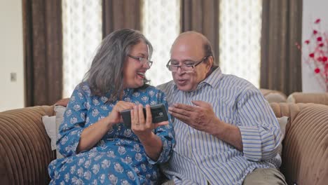 Happy-Indian-old-couple-watching-funny-video-in-mobile-phone