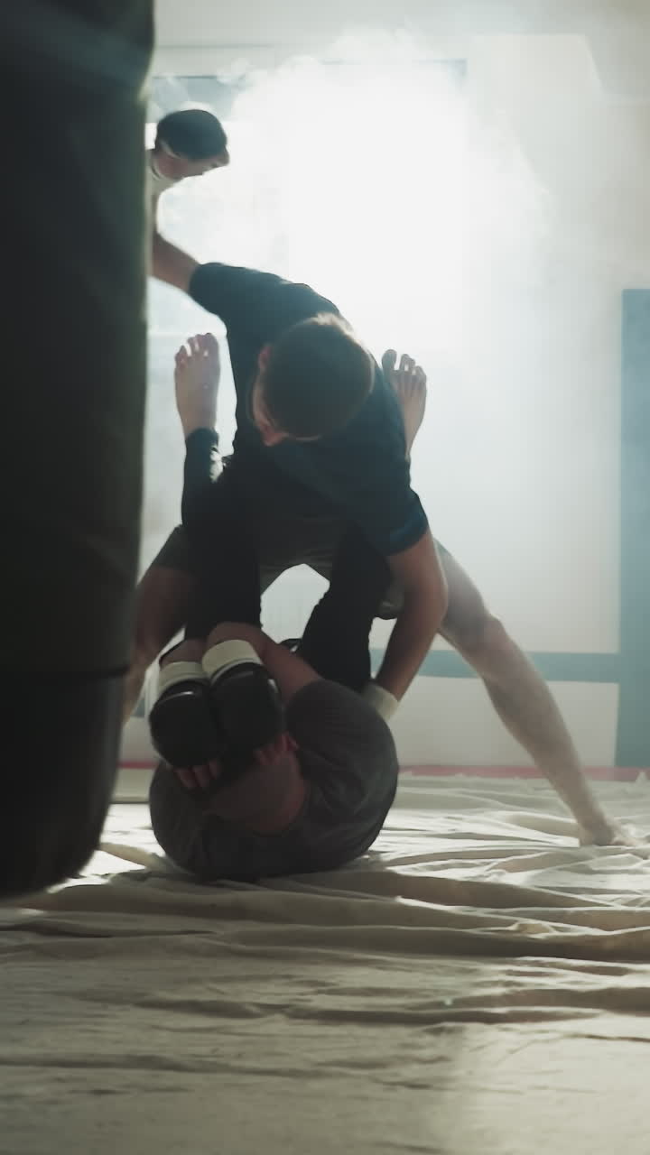 스포츠 클럽에서 바닥에 누워있는 파트너를 때리는 스포츠맨: 강한 남자가 흡연 체육관에서 스파링을 하는 친구를 때립니다.