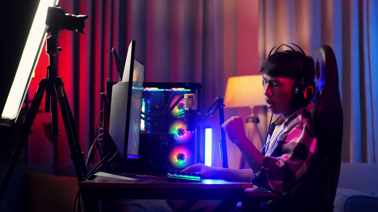 vista lateral de un niño asiático que juega a un juego en red en una computadora personal. bostezando y durmiendo, videojuego de transmisión en vivo, escritorio iluminado por luz de tira led rgb