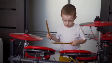 a boy plays electronic drums at home. a little boy enjoys playing the electronic, red, drum at home. the boy at home on self-isolation exercises drums
