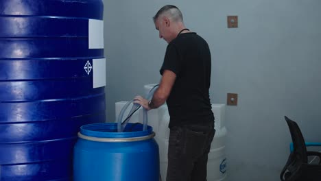 worker transferring liquid between barrels