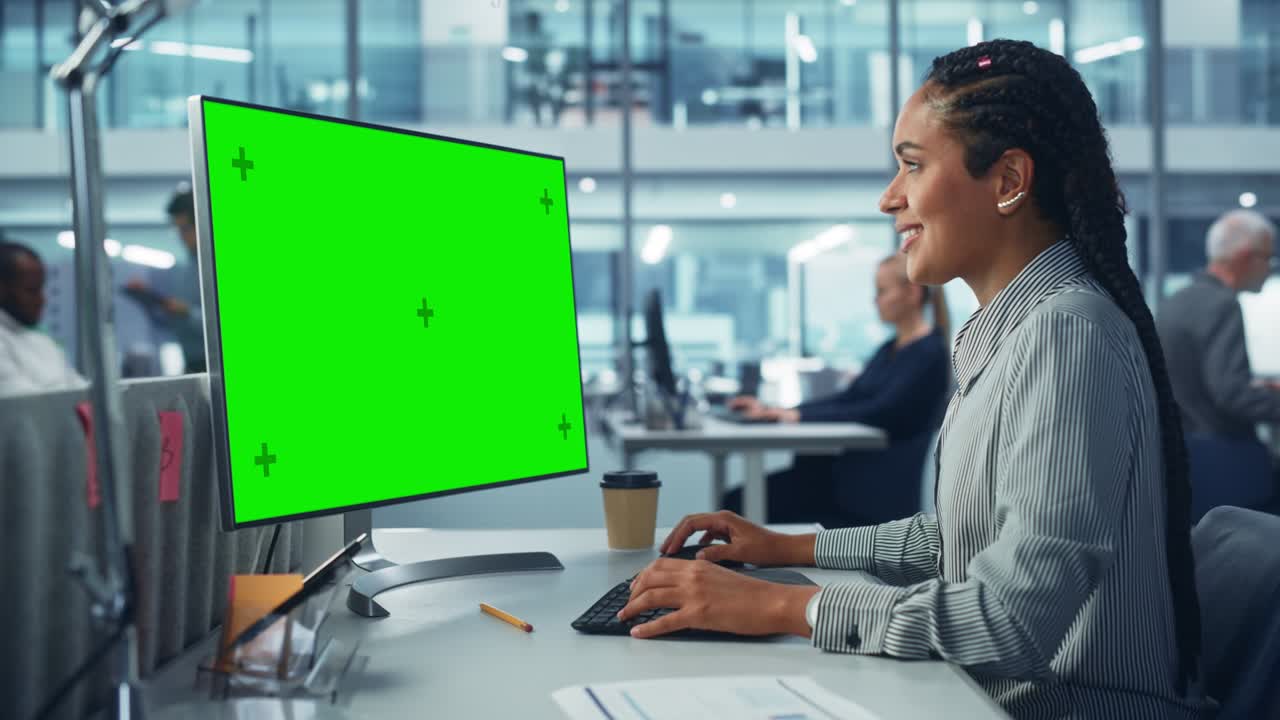 Ufficio aziendale diversificato: Bella tecnica IT donna di colore che usa un computer desktop con schermo Chroma Key verde. Ingegnere del software creativo lavora su marketing e sviluppo di progetti eCommerce