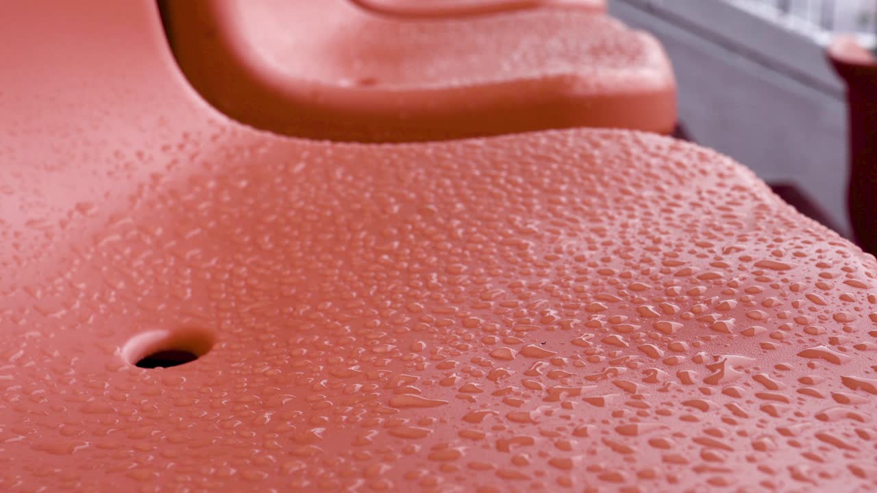 muchos asientos vacíos en el estadio en un día de lluvia. hay muchas gotas de agua en las sillas. tiro de inclinación de abajo a arriba. tiro lateral. el sujeto está a la izquierda. primer plano.