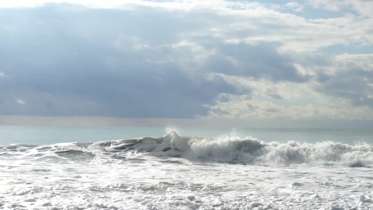 Low-angle cinematic view of powerful waves crashing on the grey, cloudy beach of England's dramatic coastline, showcasing raw nature in a textured, atmospheric scene enhanced by dynamic motion