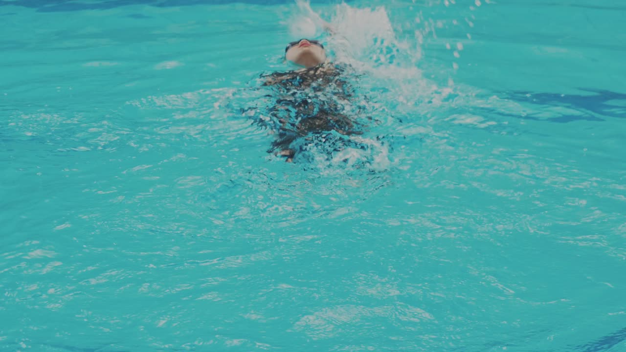 Young professional girl swimmer doing backstroke in indoor swimming pool