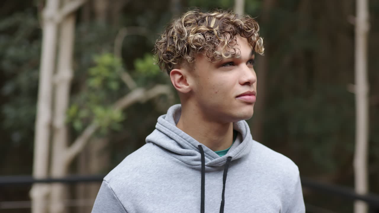 Young man in gray hoodie enjoying nature, looking thoughtful in forest