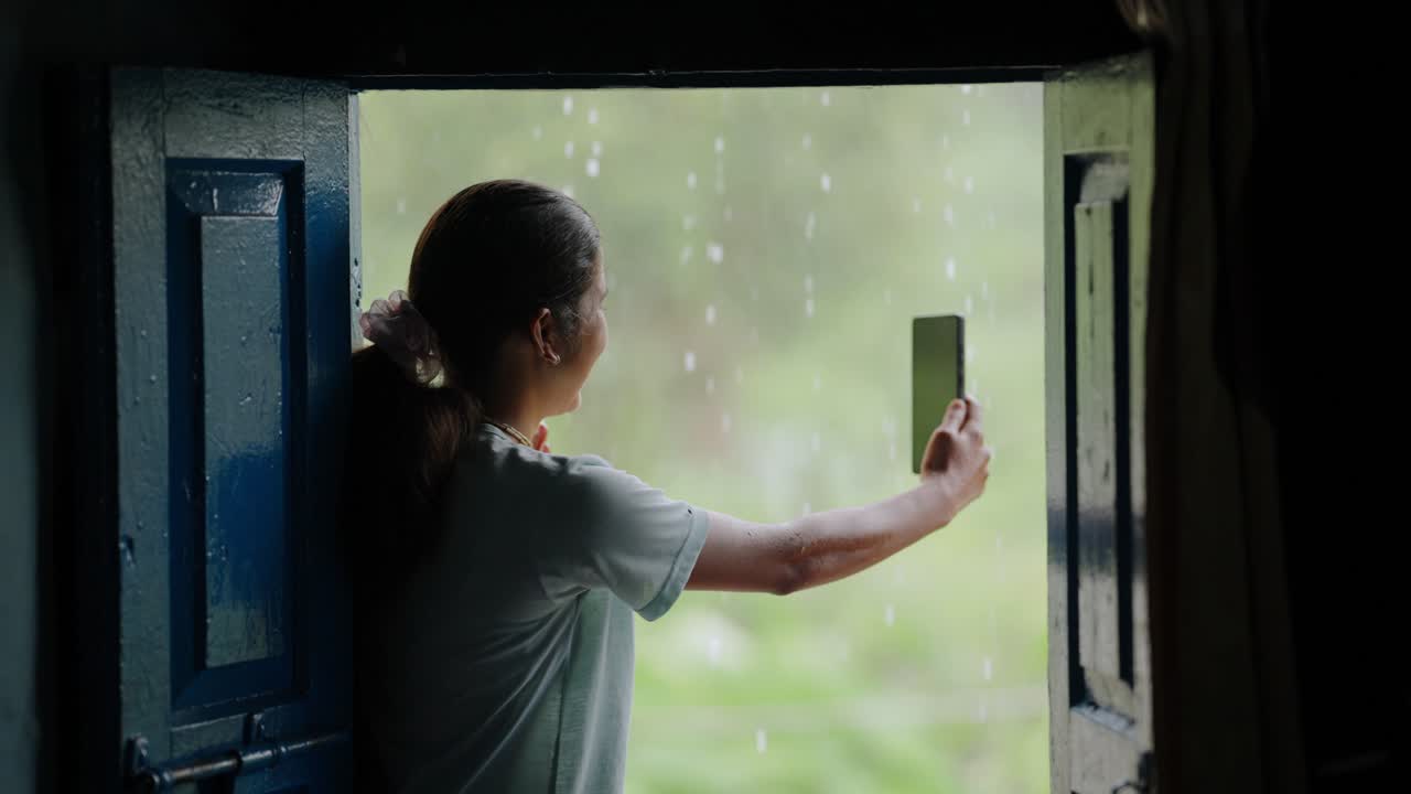Indian village child sitting at house entrance enjoying rain with soft smile, monsoon serenity, 4k video
