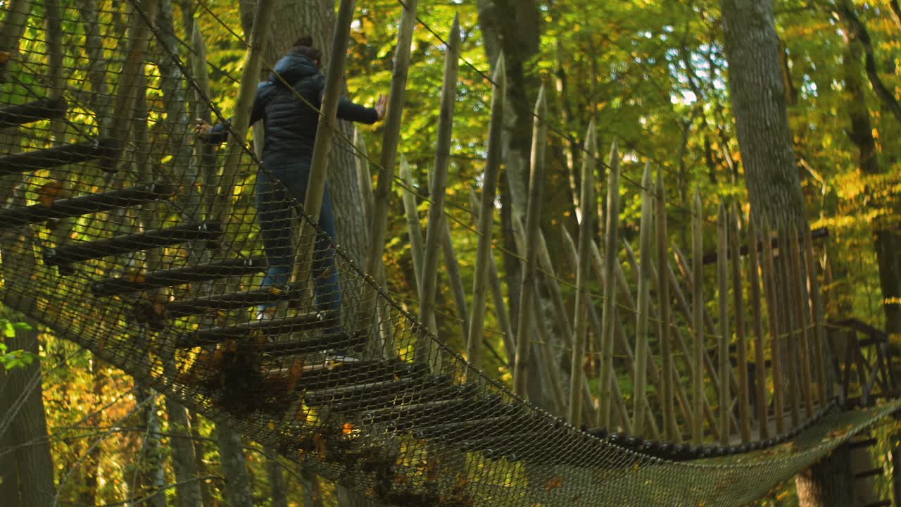 chica trepa por el puente de cuerda en un día soleado de otoño