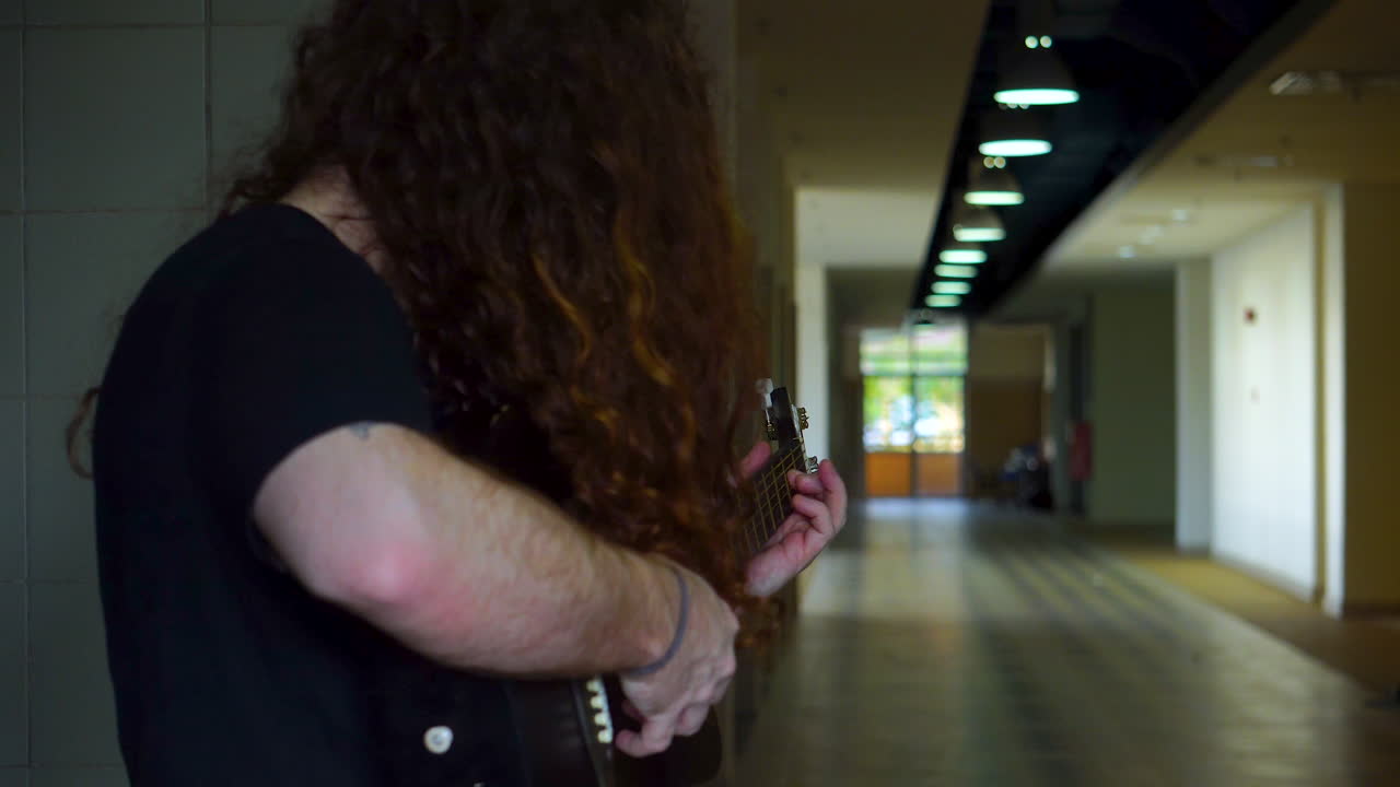 hombre de pelo largo tocando la guitarra acústica en el interior de un largo pasillo vacío y poco iluminado con iluminación bokeh