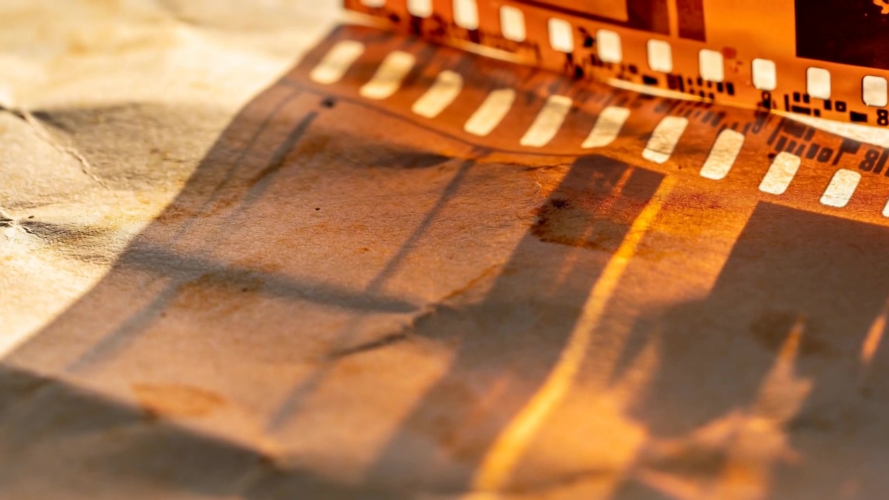 Luce calda avvolgente che rivela le ombre delle perforazioni di una pellicola da 35mm su carta stropicciata, studiando la texture.