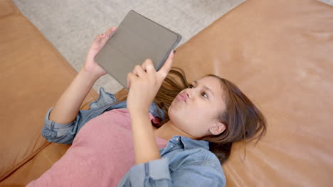 lying on couch, girl using tablet for entertainment at home