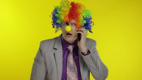 Clown-businessman-entrepreneur-boss-talking-on-mobile-phone.-Yellow-background