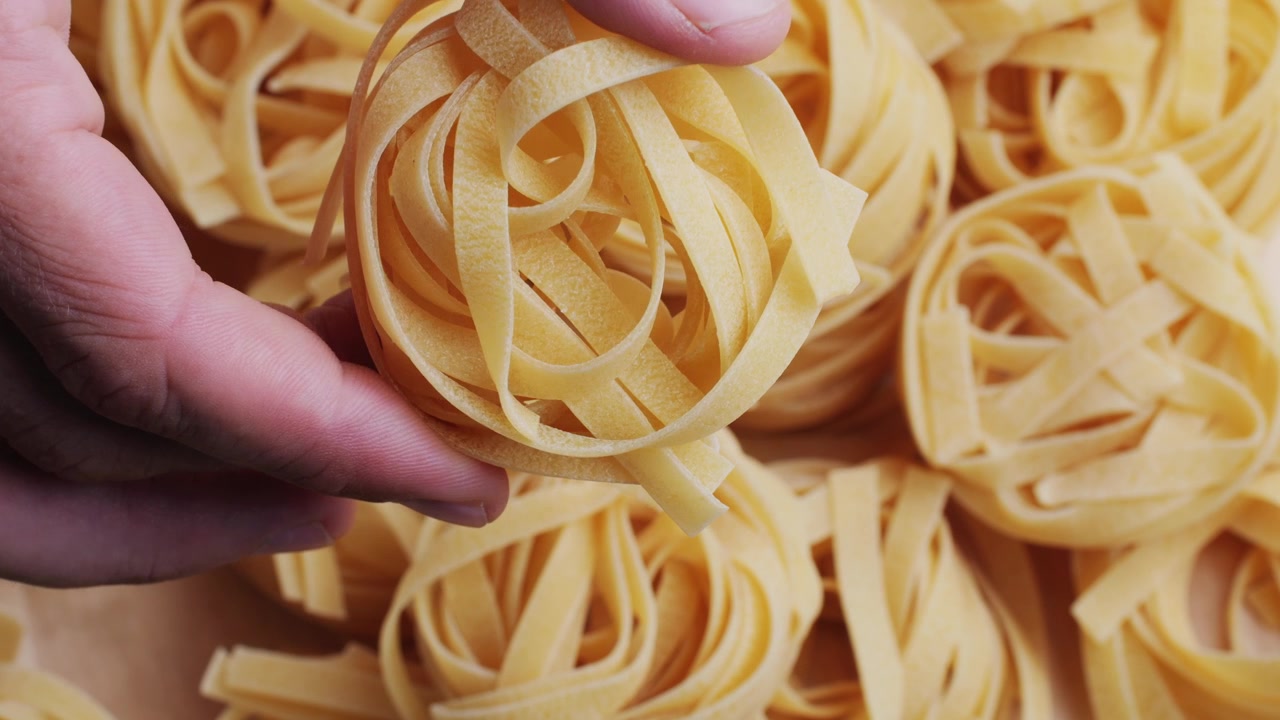 Mano che raccoglie un nido di tagliatelle crude