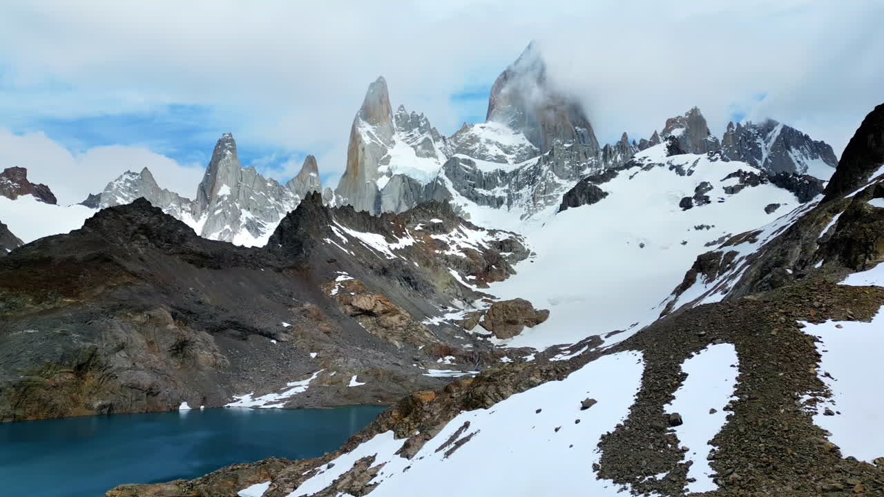 Ripresa aerea con drone delle spettacolari cime granitiche del Fitz Roy parzialmente coperte dalle nuvole, con ghiacciai che si estendono lungo i pendii al rallentatore