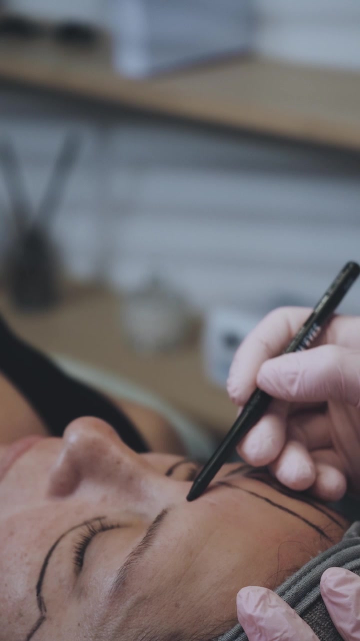 Kosmetikerin zeichnet Augenbrauen für Microblading vor