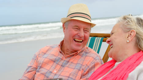 Vista-Frontal-De-Una-Pareja-De-Ancianos-Caucásicos-Usando-Una-Tableta-Digital-Y-Sentados-En-Una-Tumbona-En-La-Playa-4k