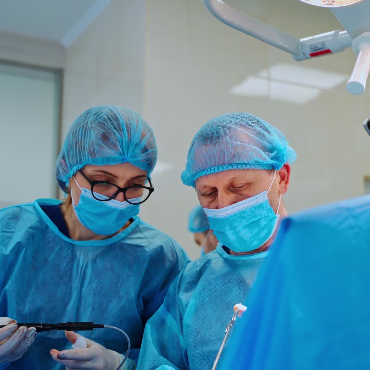 Professional nurse helps the surgeon during operation. Medical specialists in protective uniform perform a surgery in the contemporary operating room in clinic.