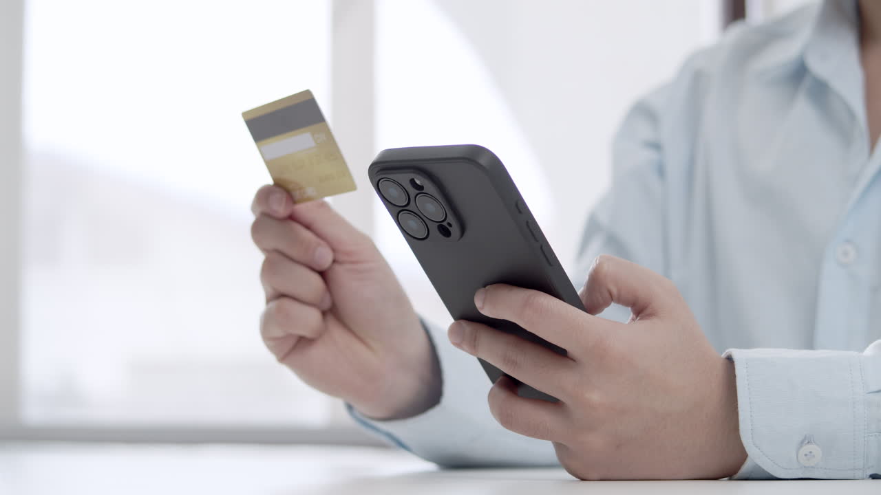 Young office worker's hands entering credit card details on a mobile phone for an online purchase, highlighting e-commerce and digital payment concepts.
