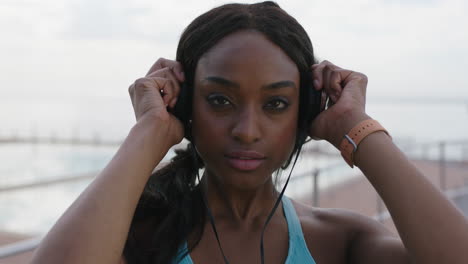 young confident athletic black woman portrait removes headphones smiling seaside