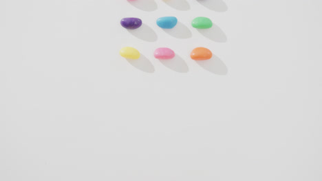 Video-of-overhead-view-of-rows-of-multi-coloured-sweets-over-white-background