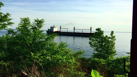Wide-shot-of-slow-moving-tanker-going-by-on-a-calm-day-on-Lake-Ontario,-viewed-from-high-vantage-point-on-shoreline
