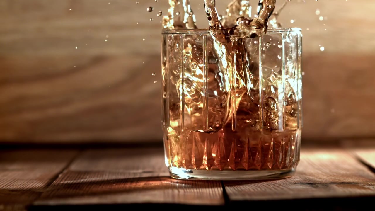Cubo di ghiaccio che cade al rallentatore in un bicchiere di whisky