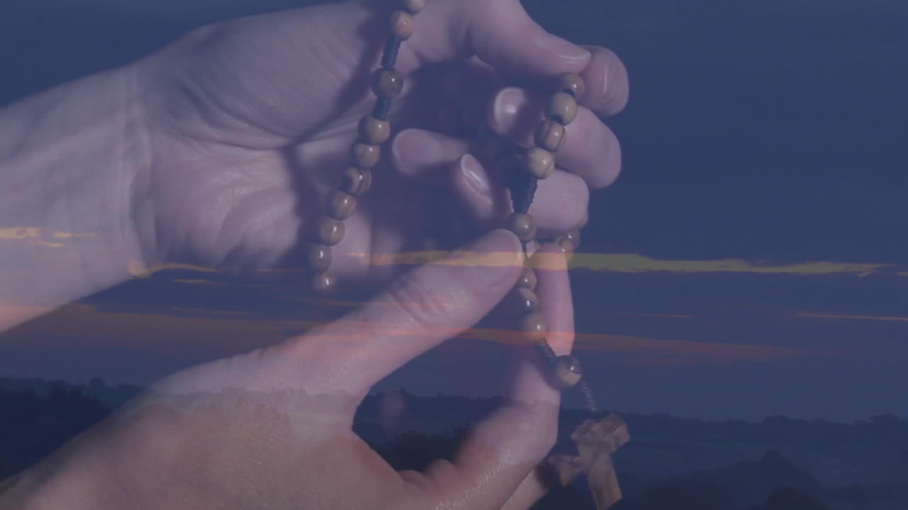 Holding prayer beads, hands reflecting in serene sunset landscape with animation