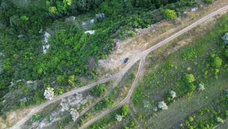 avión no tripulado dando vueltas sobre carreteras rurales y campos verdes cerca de área rocosa, detectando coche negro solitario, 4k