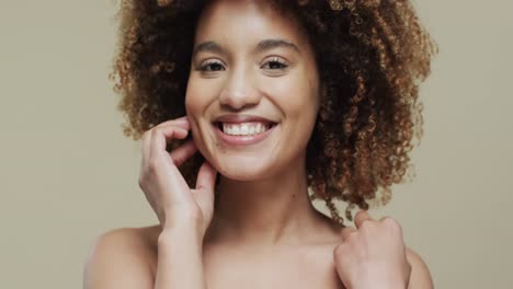happy biracial woman with dark curly hair on beige background, slow motion