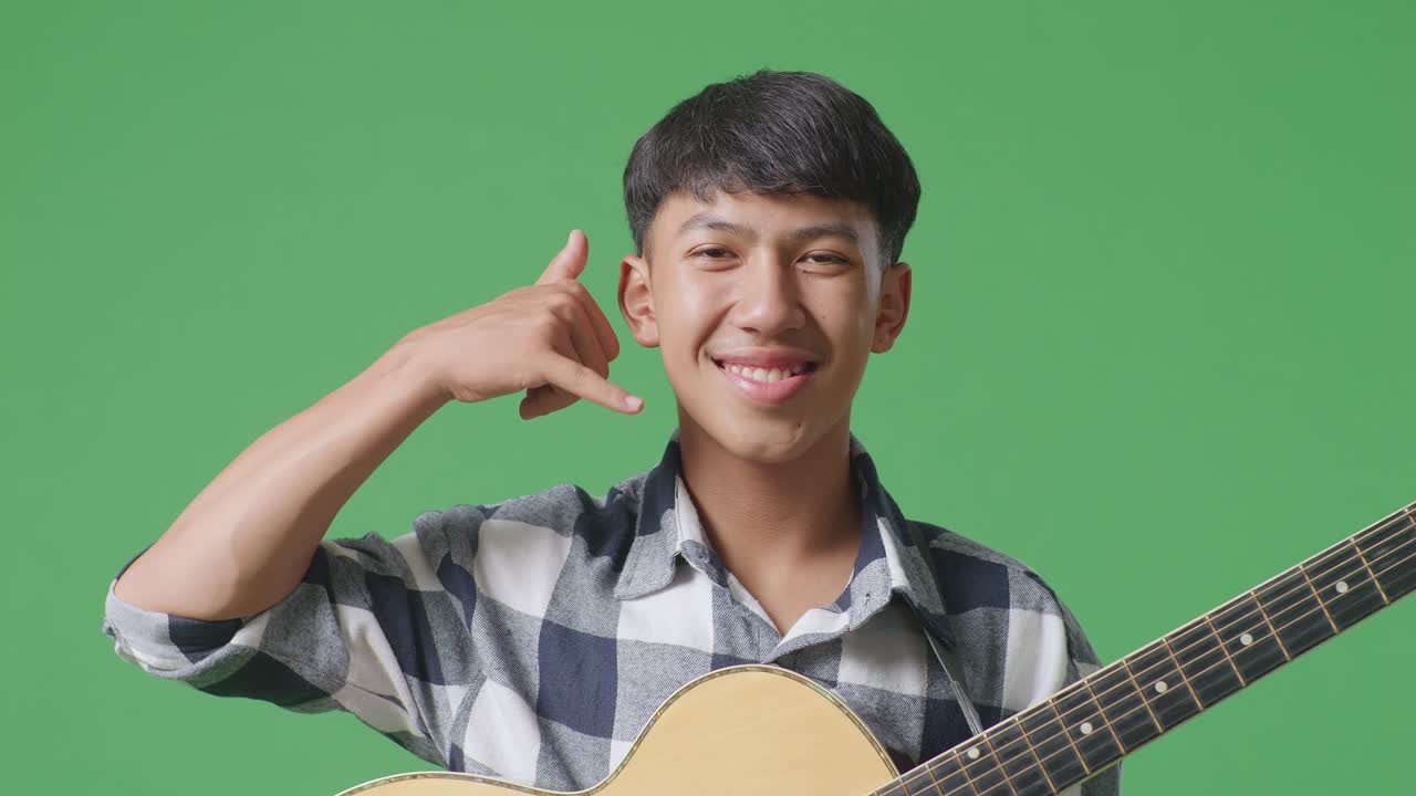 기타를 연주하는 아시아 청소년의 클로즈업은 녹색 스크린 배경에서 제스처와 웃음을 보여줍니다.