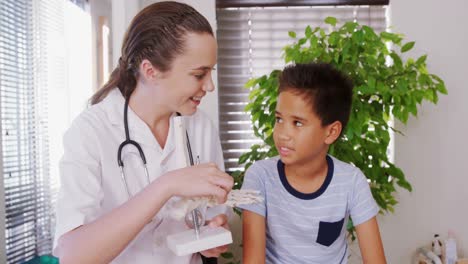 Female-physiotherapist-explaining-skeleton-model-to-boy-patient-4k