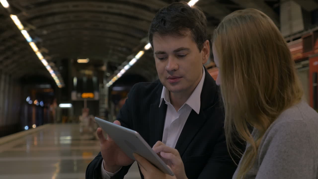 Man and woman passing time with touch pad in the underground