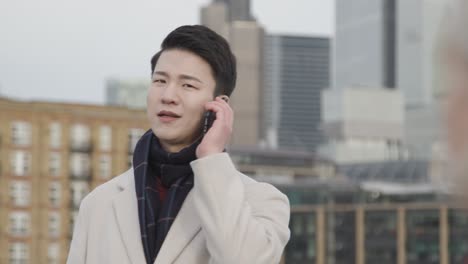 young asian businessman talking on mobile phone with london city skyline in background 2