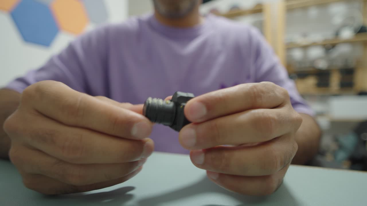 Man in purple shirt holds a novelty USB flash drive designed as a small DSLR camera, carefully revealing the plug beneath the lens