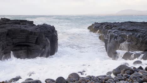 las olas chocan contra columnas de basalto volcánico en una playa islandesa, guijarros en primer plano