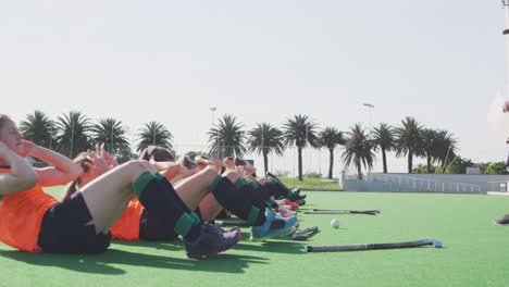 Coach-watching-female-hockey-players-exercising-on-the-field