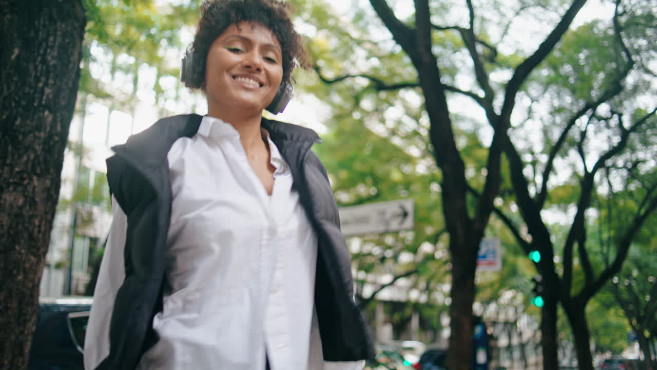 Close-up de garota ouvindo música e caminhando pela cidade com fones de ouvido. Mulher africana dançando uma canção.