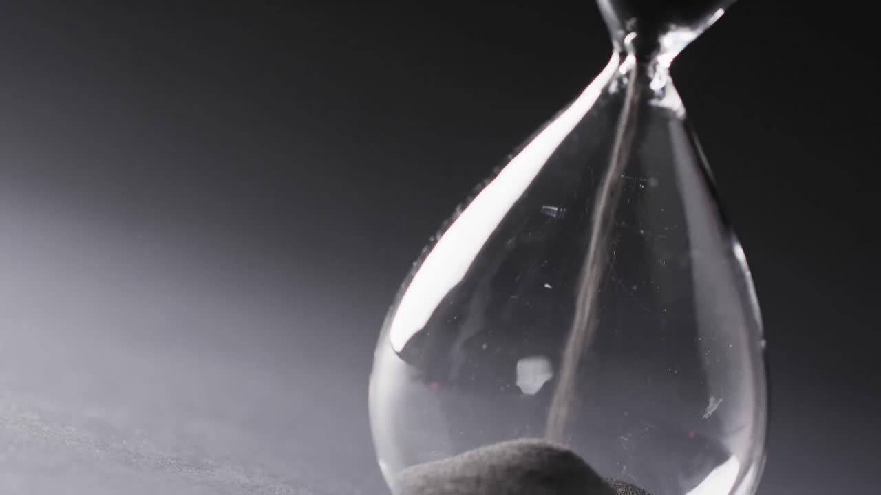 Video of hourglass with sand pouring, copy space on black background