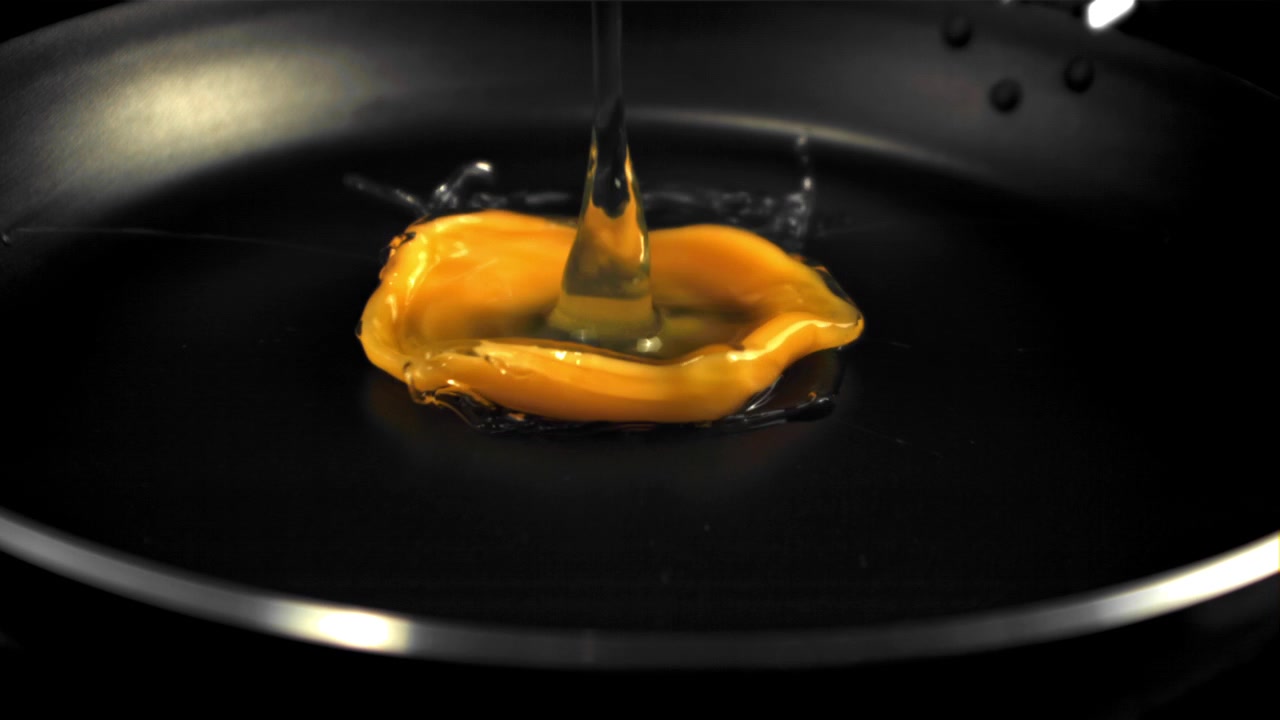 Slow motion of egg cracking and pouring into frying pan