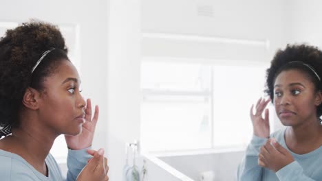 mujer afroamericana chequeando su piel, mirando la cara en el espejo del baño, cámara lenta