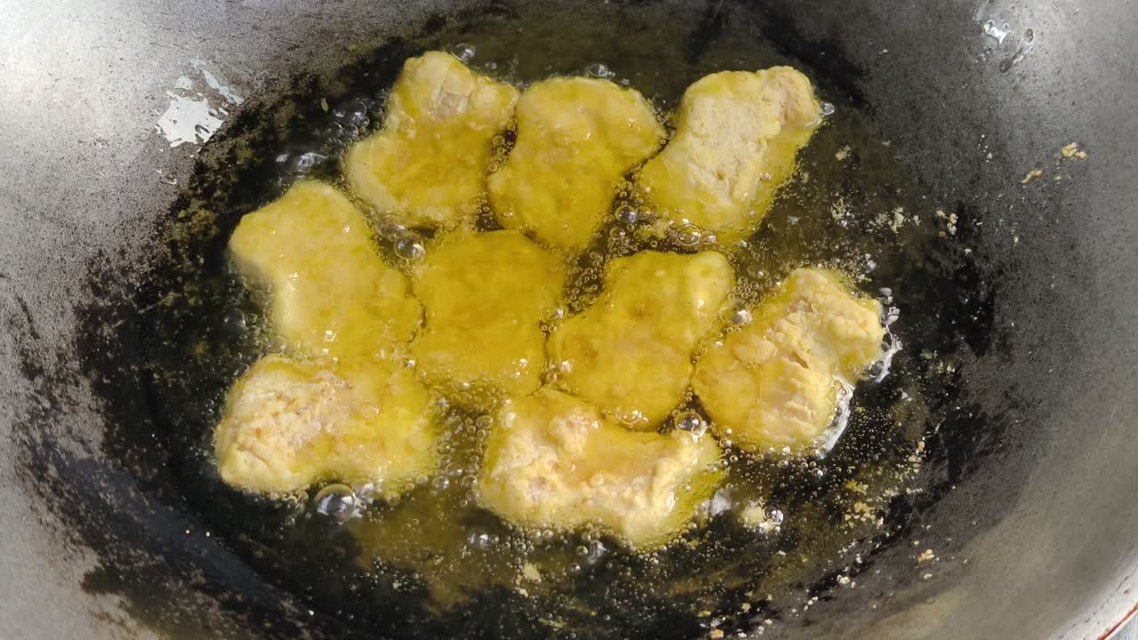 Lo chef sta friggendo bocconcini di pollo in un wok. Sta usando olio di palma e i bocconcini sfrigolano mentre cuociono nell'olio bollente