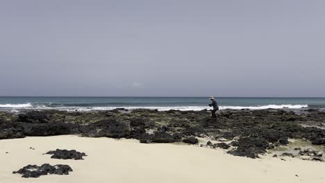 person with hat gathering mussels along the rocky shoreline of boa vista, cape verde. the scene captures the island rugged coastal environment and traditional foraging practices