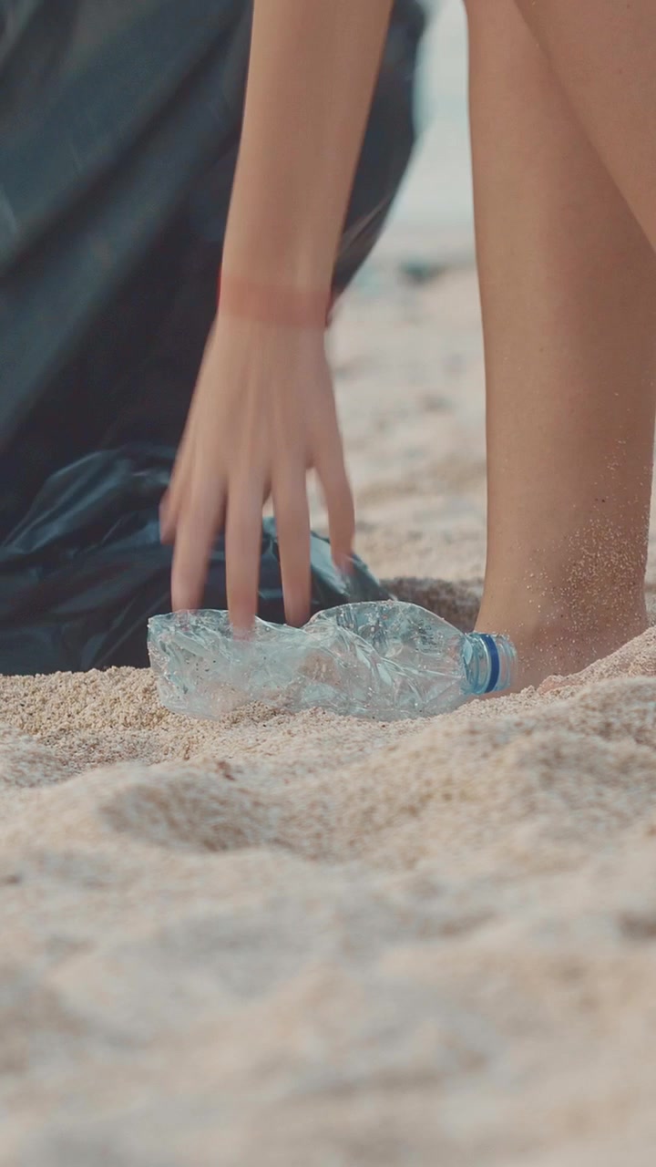Un volontario pulisce una spiaggia raccogliendo una bottiglia di plastica usata.