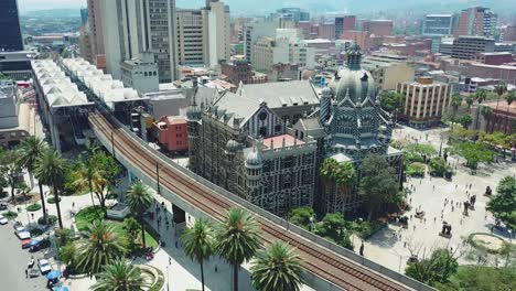 Toma-Aérea-Inclinada-Del-Centro-De-La-Ciudad-De-Medellín-Y-La-Plaza-Botero-Con-Metro-Y-Palmeras