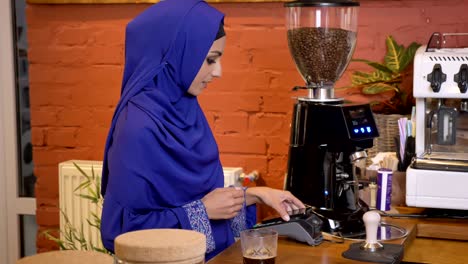 young beautiful muslim woman in hijab making contactless payment by cell phone, smiling