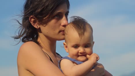 mãe e filha sentadas na praia a abraçar-se.