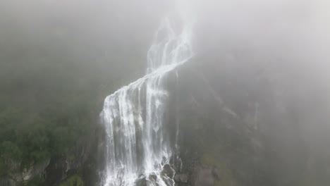 a large waterfall in a mountain between a lot of fog, norway, nature, drone