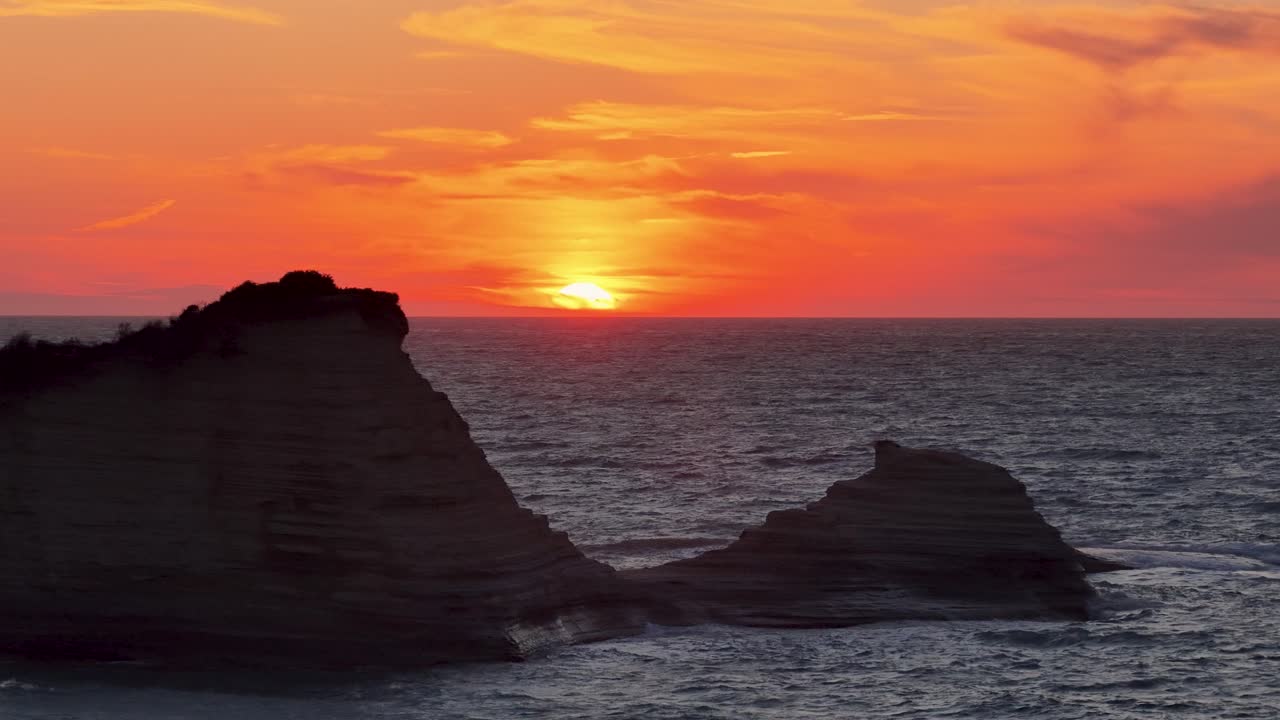 Captivating Mediterranean Sunset: The sun dips below the horizon, painting the sky in fiery orange hues, casting dramatic silhouettes of coastal rock formations against the glistening sea.