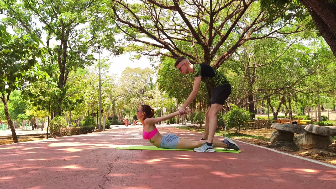 Woman practicing backbend yoga with a personal trainer in a park